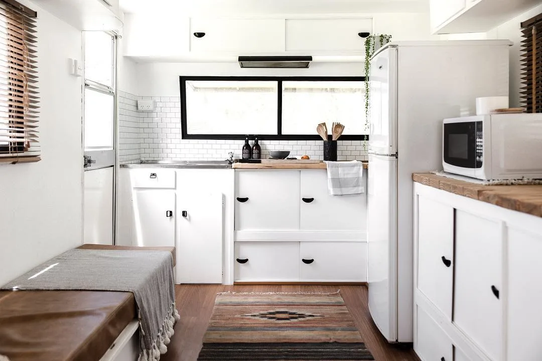 Interior of renovated travel trailer showing a white kitchen at one end of the carvavan