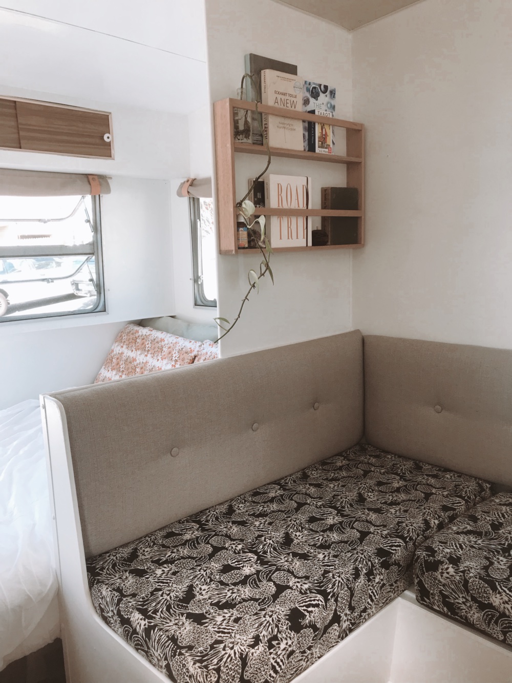 Lounge corner in a renovated travel trailer showing small shelves above the sofa.